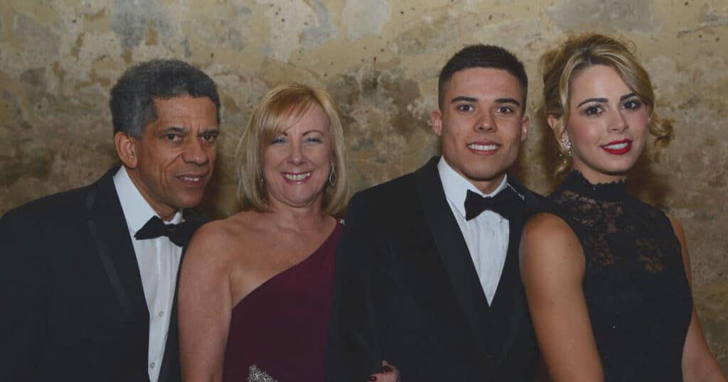 Young man with his family and partner pose for a photo at a black tie event.